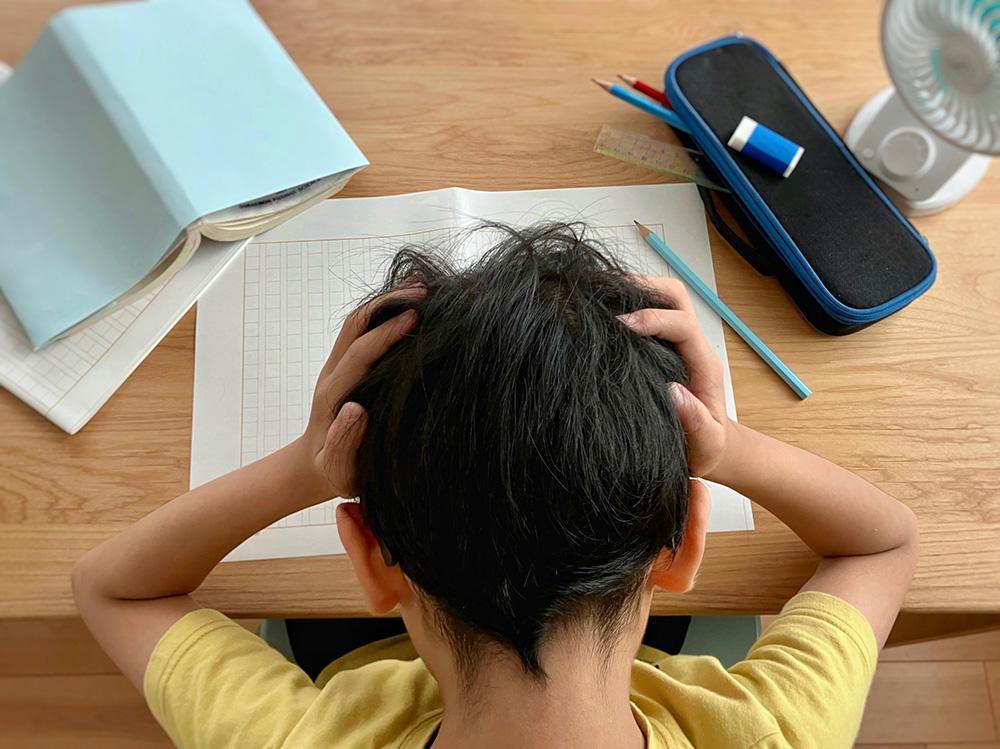 机に向かい頭をかかえる少年の様子